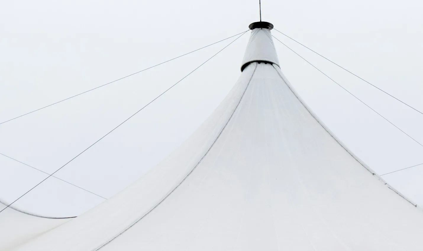 Cumbrera de una carpa blanca tensada con cables contra el cielo