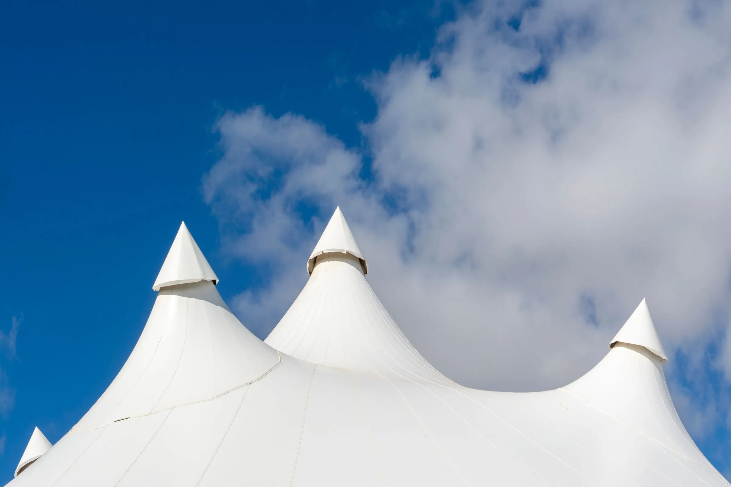 Cubierta de una carpa de gran formato con cuatro mástiles contra un cielo azul con nubes