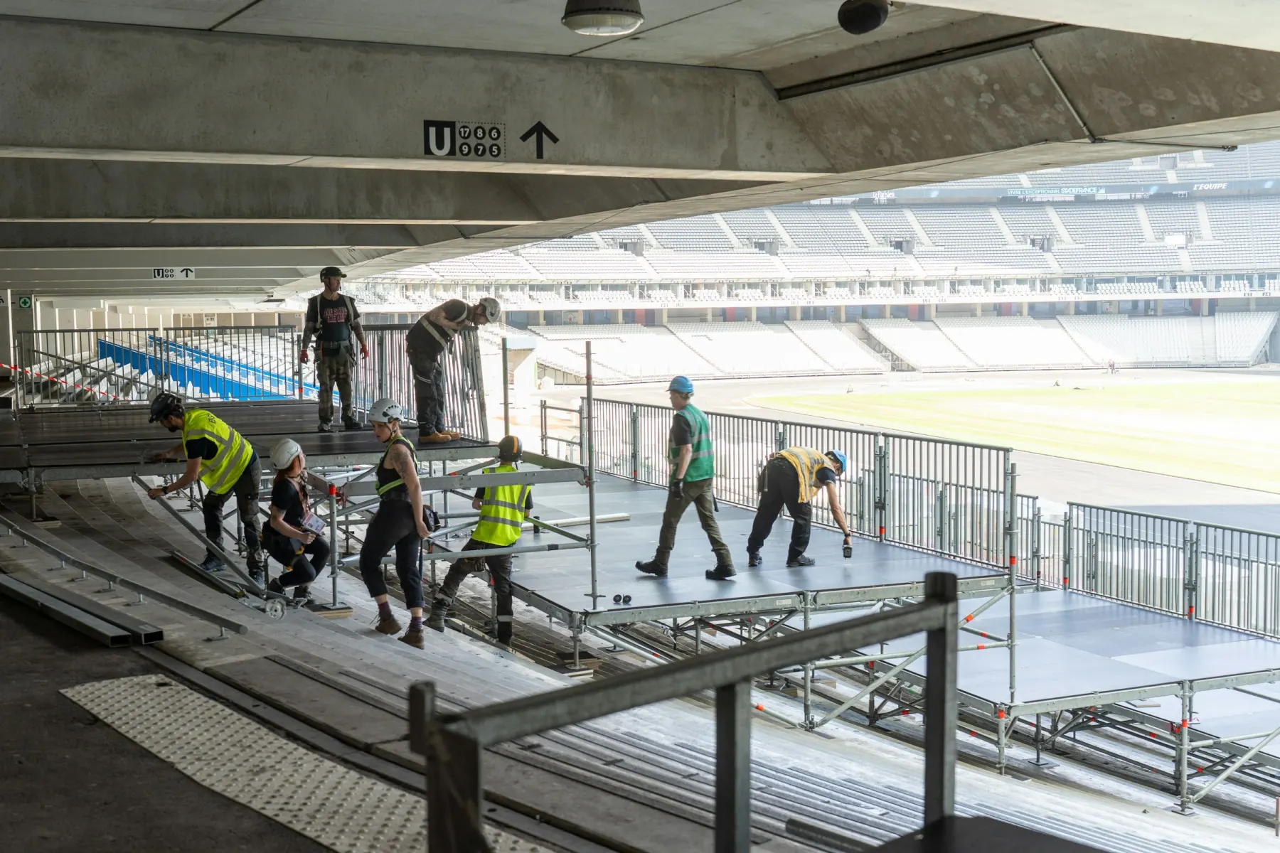 Equipo con cascos y chalecos armando plataformas modulares en un estadio